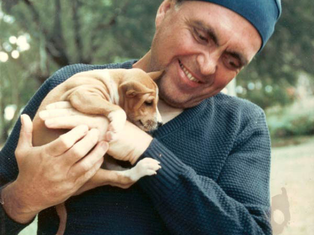 Photo of Adi Da Samraj smiling and holding a little brown puppy